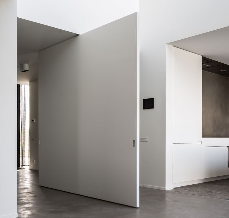 Oversized pivot door in minimalist white interior